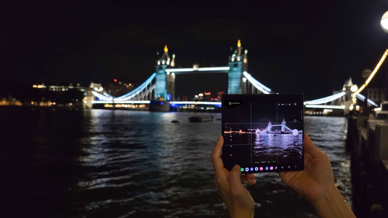 Ruce drží rozložený Samsung Galaxy Z Fold s otevřenou aplikací fotoaparátu, focení Tower Bridge v noci