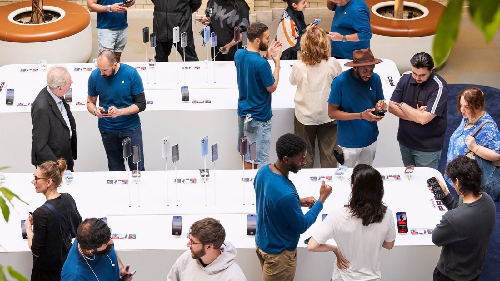 Zaměstnanci pomáhají zákazníkům u vystavených iPhonů v prodejně Apple Covent Garden